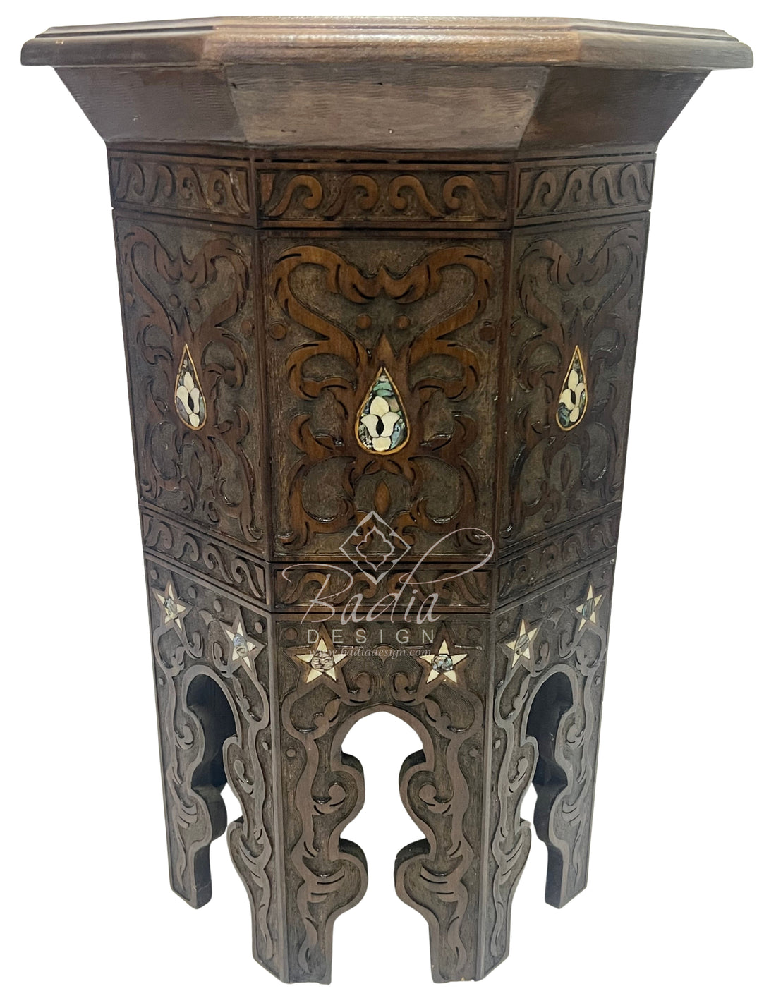 Decorative wooden side table with intricate carvings and Badia Design Inc branding.